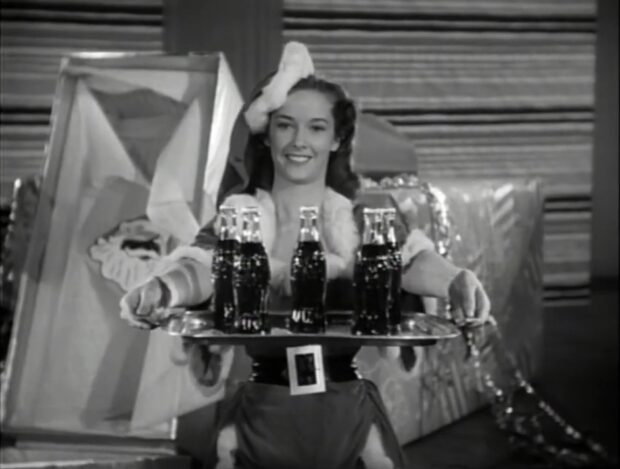 Vera Miles carries a tray of Coca Cola while dressed as a Santa Belle